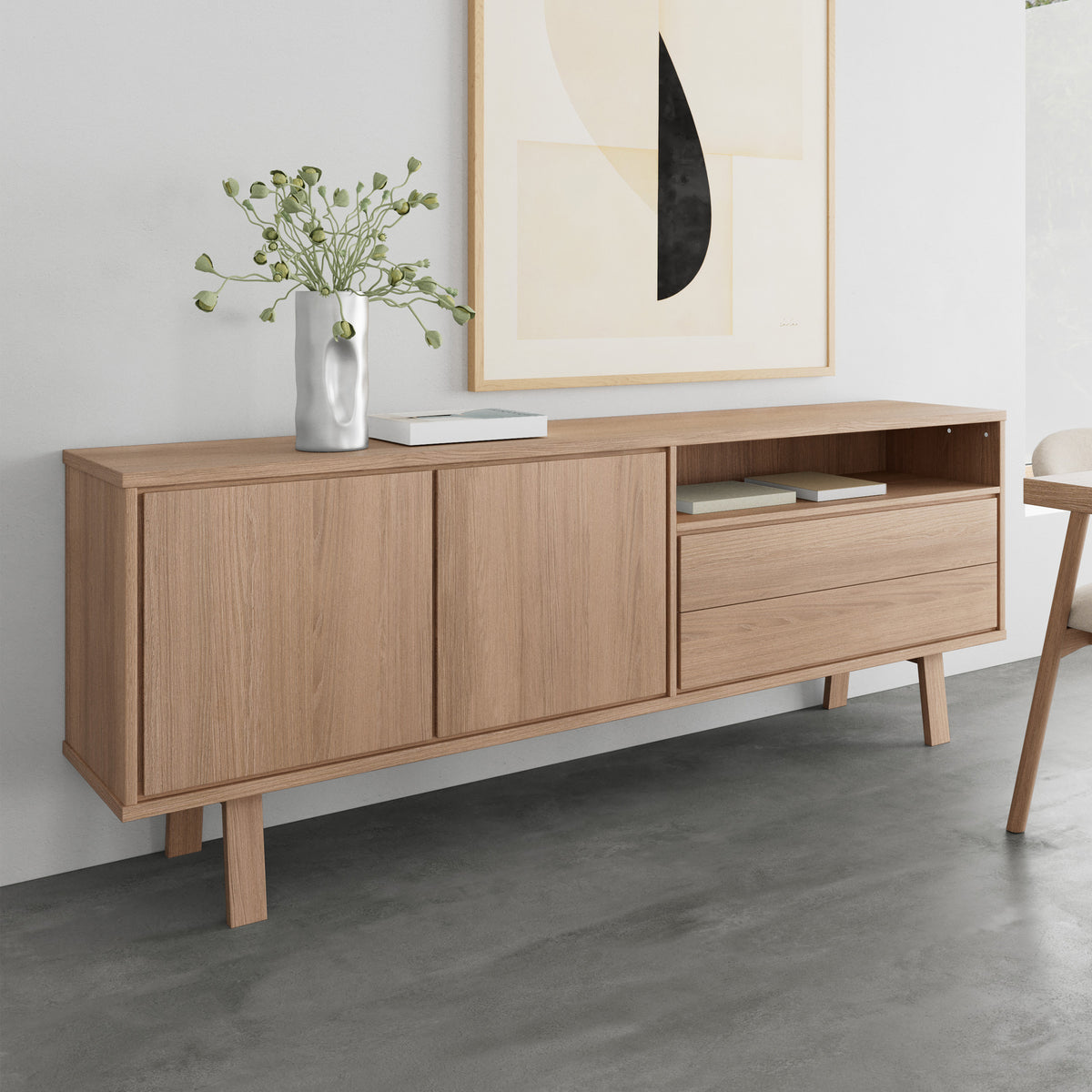 Commode Lurisse 200 x 75 en chêne blanchi, placée devant une illustration contre un mur gris, avec un vase et des livres – commode pour le salon