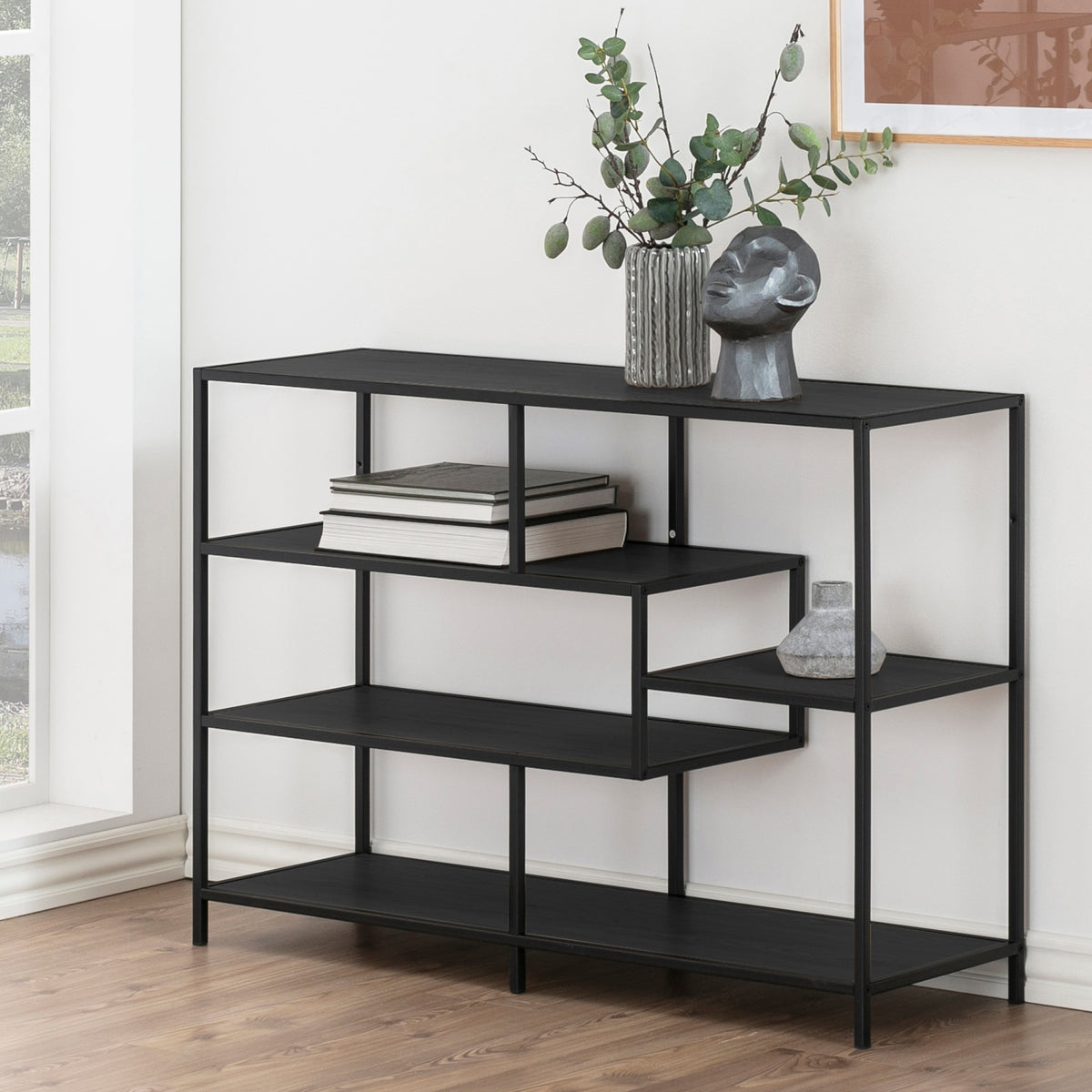 Étagère Skeleto 114 x 78 en mélamine noire près d'une fenêtre, avec des brindilles dans un vase, une sculpture et des livres – étagère noire pour le salon