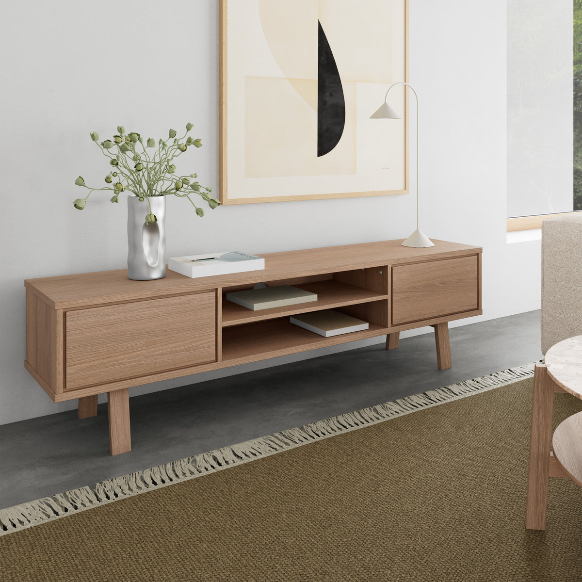 Meuble TV Lurisse 180 x 50 en chêne blanchi dans le salon, sous une affiche, avec une lampe, un vase et des livres, sur un tapis couleur olive