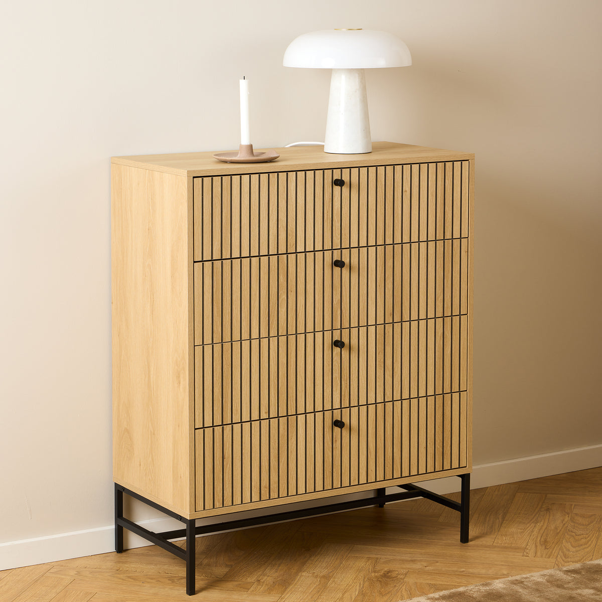 Commode Bambouz 81 x 100 devant un mur beige, avec une lampe blanche et une bougie sur un parquet à motif en chevrons – commode pour chambre à coucher