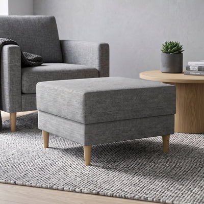 Pouf Harmi 66x66 dans un salon devant un fauteuil gris, à côté d'une table ronde avec une plante grasse – pouf pour le salon