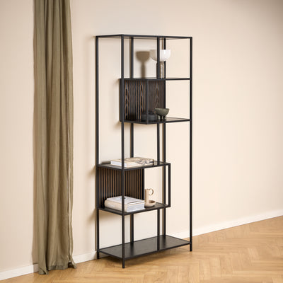 Étagère Skeleto 77 x 185 en mélamine noire, placée contre un mur clair à côté d'un rideau en lin, avec des objets en céramique et des livres sur les étagères
