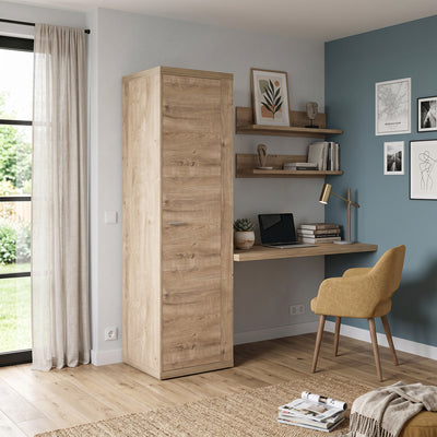 Kledingkast Korin 201x57 in een lichte kamer met blauwe muur, naast planken en fauteuil – smalle kast voor kleine woning