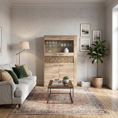 Vitrinekast Korin 102x160 in de woonkamer met grijze bank en oosters vloerkleed – vitrinekast met glazen
